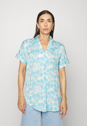 Camisa de manga curta floral azul claro em tecido suave, com gola em notch e bainha curva, apresentando padrões de flores azuis e brancas.