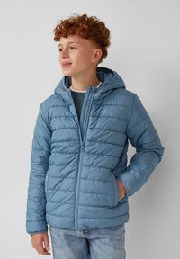 Helle blaue Winterjacke mit Kapuze, horizontalen Nähten, einem Reißverschluss auf der Vorderseite und seitlichen Taschen. Über einem geschichteten Outfit getragen.