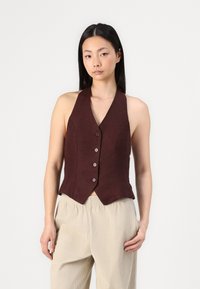 Gilet di lino bordeaux con un design aderente, scollo a V profondo e chiusura con cinque bottoni. Abbinato a pantaloni beige a vita alta con pieghe a gamba larga.