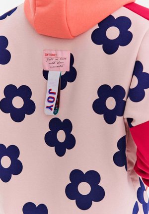 Hoodie w jasnoróżowym kolorze z dużym ciemnoniebieskim wzorem kwiatowym. Posiada koralowe akcenty na ramieniu oraz metki z logo. Miękka tekstura.