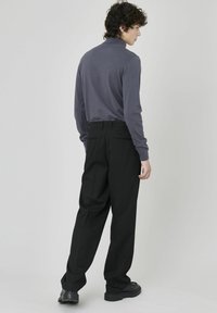 Polo gris à manches longues avec un col haut associé à un pantalon noir ajusté, présentant une coupe droite et un tissu légèrement texturé.
