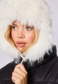 Schwarze Daunenjacke mit einer weißen Kunstpelzkapuze. Der Pelz ist flauschig und voluminös und wird durch einen Kordelzug am Hals ergänzt.