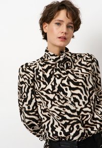 Zwart-witte blouse met een zebra-print patroon, pofmouwen, een hoge kraag en een strikdetail bij de halslijn. Geverfde stof.