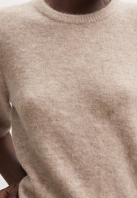 Beige Pullover aus Wolle mit Rundhalsausschnitt, kurzen Ärmeln und einer weichen, flauschigen Textur. Der Stoff wirkt leicht und bequem und zeigt ein dezentes Muster.