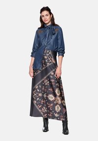 Denim blouse with bow detail, paired with a patterned maxi skirt featuring floral designs in red, cream, and navy. Black ankle boots complete the look.