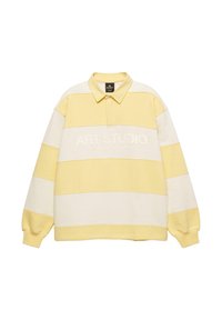 Polo à manches longues rayé jaune et blanc avec col et texte brodé « ART STUDIO Creative Department ». Texture de tissu doux.