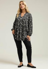 Blusa nera a fiori con maniche lunghe e scollatura a V, abbinata a pantaloni neri slim-fit e ballerine nere con un accento decorativo.