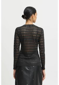Sort blonde langærmet top med en scallop-kant, der har et bladmønster og en tætsiddende silhuet, båret over en sort læderskirt med detaljer.