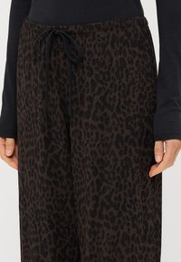 Pantaloni con stampa leopardata nera e marrone, dotati di vita con cordino. Il tessuto sembra soffice; il design ha una vestibilità ampia con tasche laterali.