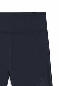 Close-up of navy blue leggings showing high waistband and panel stitching details.