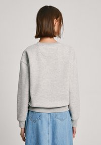 Sudadera gris con cuello redondo y puños acanalados, con un corte relajado y una textura suave. La parte posterior tiene un sutil detalle de costura.