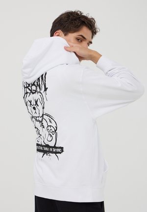 Felpa bianca con un design grafico nero di un orso cartoon sulla schiena e la scritta "PENSIERI POSITIVI NELLA MENTE." Materiale in cotone.