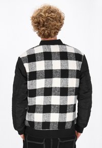 Sweter w czarno-białą kratę z dzianym tyłem i rękawami przypominającymi skórę. Posiada prążkowany kołnierz i mankiety oraz luźny krój.