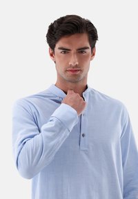 Camicia a maniche lunghe, di colore blu chiaro, con colletto alla cinese, dotata di un placket con bottoni e maniche con polsini, realizzata in un tessuto liscio.