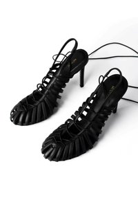 Scarpe nere con tacco alto, dotate di cinturini in pelle incrociati e design con punta aperta. Presentano un interno imbottito e un tacco sottile e slanciato.