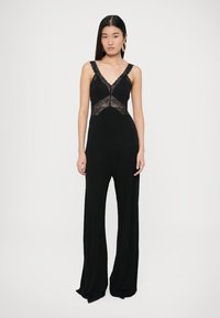 Czarny kombinezon z miękkiej tkaniny, z koronkowymi detalami na dekolcie, szerokimi nogawkami oraz cienkimi ramiączkami i dekoltem w kształcie litery V.