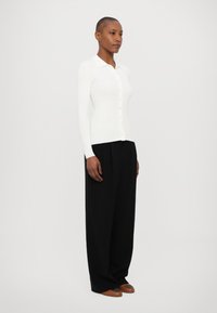 Witte geribbelde lange mouwen cardigan met kraag, knoopsluiting aan de voorkant, gecombineerd met zwarte wijd-uitlopende broek en bruine schoenen.