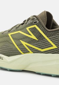 Chaussure de course en mesh vert olive avec logo New Balance jaune et semelle intermédiaire blanche amortissante.