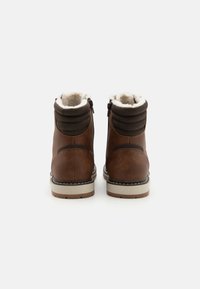 Botas de cuero marrón hasta el tobillo con un collarín acolchado marrón, forro blanco y una suela clara que presenta una costura decorativa a lo largo del borde.