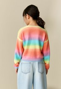 Jersey a rayas coloridas en tonos pastel de rosa, naranja, amarillo, verde y azul; textura suave con puños y bajo acanalados. Combinado con denim claro.