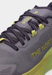 Κοντινό πλάνο γκρι και κίτρινου αθλητικού παπουτσιού The North Face με μαύρα υφασμάτινα κορδόνια και ετικέτα "MESA" στη γλώσσα.