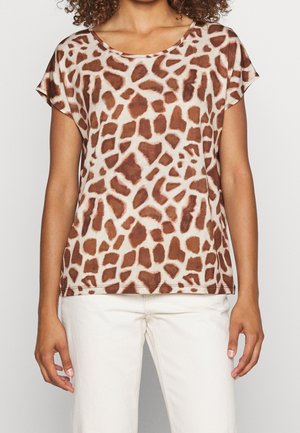 Vrouw draagt een top met korte mouwen en ronde hals met een onregelmatige dierenprint in bruin en wit, gecombineerd met witte broek.