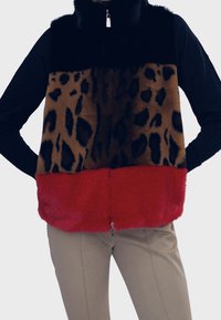 Vesta z umělého kožíšku s černou horní částí, středem se zvířecím vzorem a červeným spodkem. Zapínání na zip, vysoký límec a měkká textura.