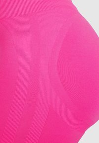 Leggings ajustados de cintura alta en tejido rosa brillante con textura acanalada y detalles suaves, que muestran un diseño atlético con patrones distintos.