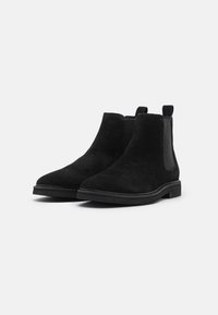 Botas de tobillo de ante negras con paneles elásticos en los laterales, punta redonda y con un mínimo de agarre en la suela plana. Estilo campestre con lengüetas para facilitar el calzado.