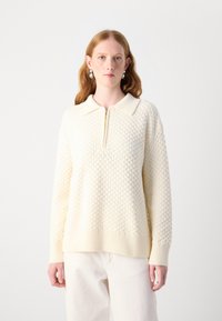 Maglione color crema con un motivo texturizzato a nido d'ape, orlo a coste e colletto. Presenta una chiusura a mezza zip sul davanti.