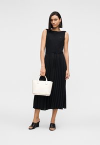 Μαύρο πλισέ μάξι φόρεμα με εφαρμοστό μπούστο, σφιχτή μέση και αμάνικο σχέδιο. Συνδυάζεται με λευκή τσάντα χειρός και μαύρα σανδάλια slide.