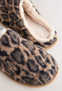 Chaussons à imprimé léopard avec une texture douce et pelucheuse, base beige et taches noires. Intérieur doublé de fausse fourrure légère pour le confort.