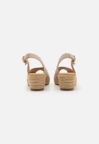 Sandalias de cuña beige con un tacón de paja texturizada, correa al tobillo con hebilla y diseño de espalda abierta. Material suave con detalles de costura mínimos.