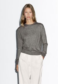 Maglietta a maniche lunghe grigia in maglia con scollo rotondo, caratterizzata da una vestibilità rilassata e orlo a costine. Abbinata a pantaloni sartoriali color bianco sporco.
