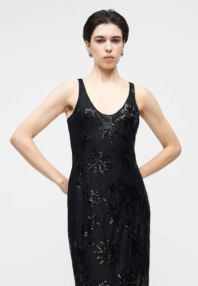 Robe noire avec un col en V profond, ornée de motifs d'étoiles complexes en sequins, présentant une coupe ajustée et une texture lisse.