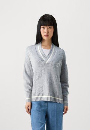 Maglione grigio lavorato a maglia con scollatura a V e bordi a coste bianchi a contrasto. Presenta scritte testurizzate e maniche larghe e rilassate.