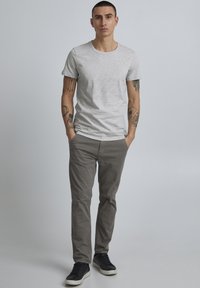 Harmaa raidallinen lyhythihainen t-paita yhdistettynä slim fit -vaaleanharmaisiin housuihin. Mustat lenkkarit valkoisilla päillä. Yksinkertainen, käytännöllinen muotoilu.