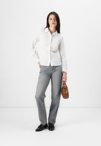 Camisa blanca de botones de manga larga, pantalones grises de pierna ancha, zapatos negros y un pequeño bolso marrón. Tejido suave y corte entallado.