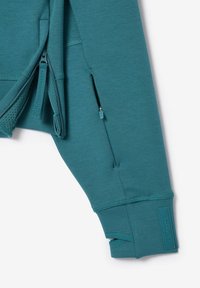 Sweatshirt teal avec une poche zippée, des accents texturés et des poignets côtelés. Il présente une doublure élégante et respirante. Le tissu présenté est lisse.
