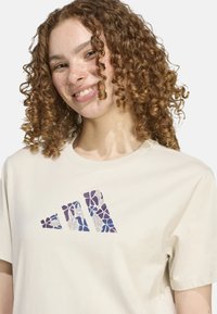 Camiseta de algodón color crema con un logo abstracto de patrones multicolores en la parte delantera. Manga corta y escote redondo.