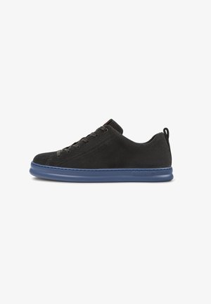 Black suede sneaker featuring a blue rubber sole, round toe, six eyelets for laces, and a rear pull tab. Clean, minimalistic design.