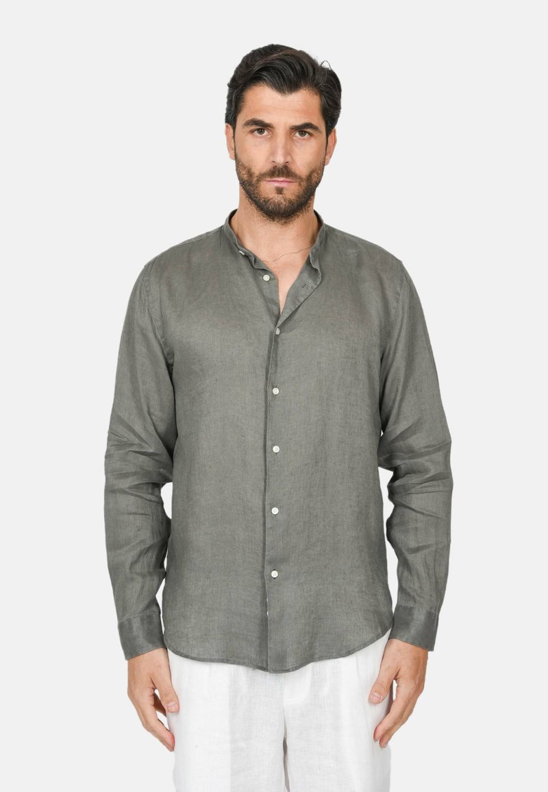 Camicia di lino grigia con una leggera texture, colletto alla mandarino e chiusura con bottoni. Maniche lunghe e vestibilità morbida, abbinata a pantaloni bianchi.