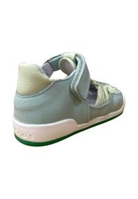 Zapato de cuero azul claro con suela de goma blanca y acentos verdes. Presenta una correa de Velcro y un diseño abierto para la transpirabilidad. Parte trasera texturizada.
