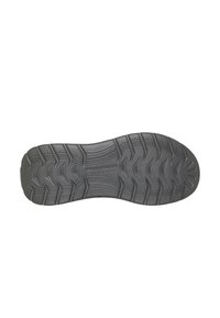 Suela de zapato de goma negra con un diseño texturizado que presenta un patrón de zic-zac y marca embossada en el centro. Es plana y ancha.