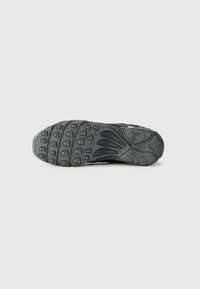 Suela de zapato deportivo negro con un diseño de goma texturizada, presentando patrones de agarre y una sección de entresuela suave.