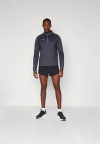 Férfi sportos ruházat sötétszürke, hosszú ujjú, cipzáros felsővel, fehér díszítéssel, fekete rövidnadrággal és sportcipővel.