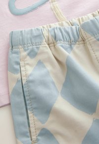 Primo piano di pantaloncini con fascia elastica con grande motivo a losanghe blu e bianche su sfondo di tessuto rosa.