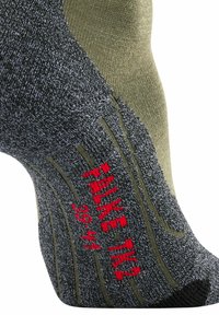Calcetín gris y verde olivo con tela texturizada y talón reforzado. Presenta el texto rojo "FALKE TK2" y marcas de tamaño.