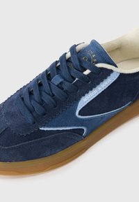 Navy blå suede sneakers med lyseblå detaljer, runde snørebånd, syede detaljer og en gummisål. Har brandlogoet på tungen.