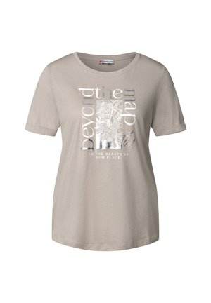 T-shirt beige a maniche corte con scollatura rotonda. Presenta una stampa grafica con dettagli argentati e il testo: "oltre la mappa" e "nella bellezza di nuovi luoghi."